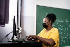 Mature teacher using a computer in the classroom - using a face mask