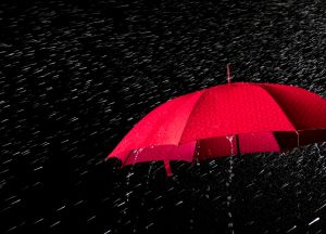 Open umbrella with raindrops falling from the sky on a black background.