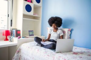 Teen girl studying with laptop in bed