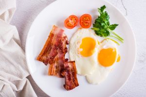 Fried eggs and bacon, tomatoes and parsley on a plate. Homemade breakfast. Top view. Closeup
