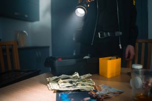 Stack of money on a kitchen table in a dark room illuminated by a flashlight light in officer's hand