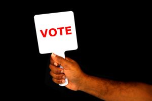 VOTE hand holding sign board with black background close-up view copy space