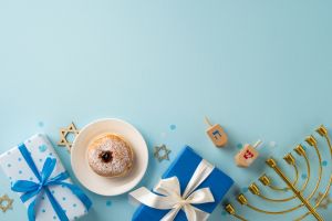 Festive Hanukkah scene featuring blue gifts, dreidels, a menorah, and a doughnut on a light background. Perfect for celebrating the Jewish holiday with warmth and joy