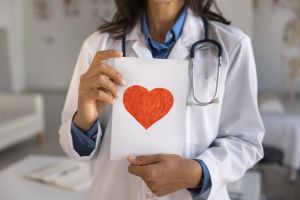 Female cardiologist holding postcard with drawn red heart symbol